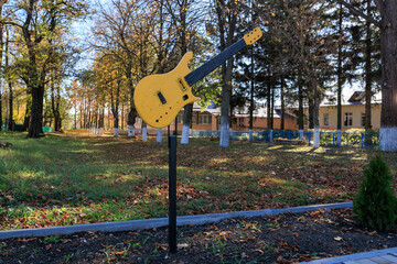 A yellow guitar is on a post in a park