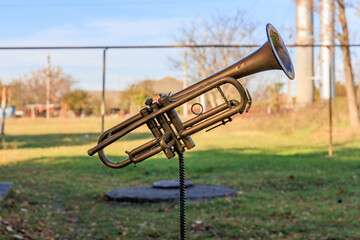 A brass trumpet is sitting on a post in a grassy field