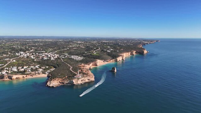 Aerial shot of the cape with a lighthouse and two sailing boats in the foreground. Algarve coast, Portugal 