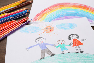 Cute child`s drawings and colorful pencils on wooden table