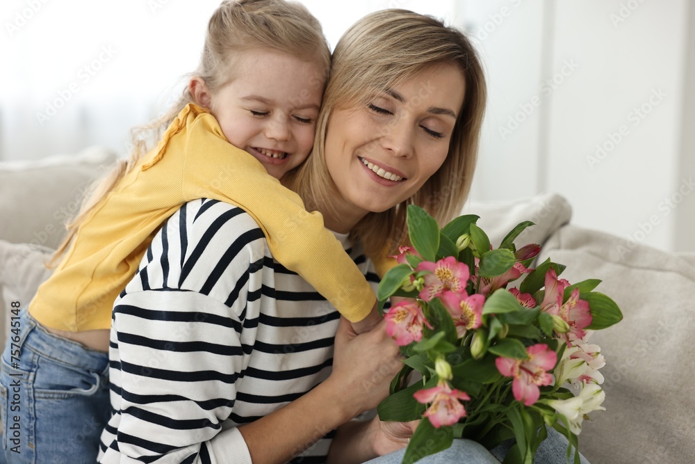 Poster Little daughter congratulating her mom with Mother`s Day at home. Woman holding bouquet of alstroemeria flowers