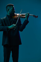 Elegant musician in black suit playing violin on vibrant blue background in artistic performance...