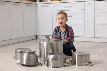 Little boy pretending to play drums on pots in kitchen