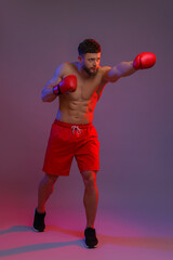 Man in boxing gloves fighting on color background