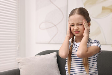 Little girl suffering from headache on sofa indoors. Space for text