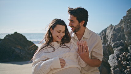 Young couple enjoying pregnancy relaxing on ocean coast summer weekend close up.