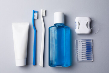 Flat lay composition with fresh mouthwash in bottle and other oral care products on grey background