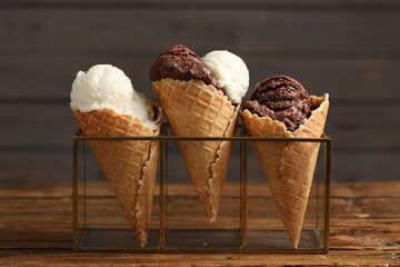 Tasty ice cream scoops in waffle cones on wooden table, closeup