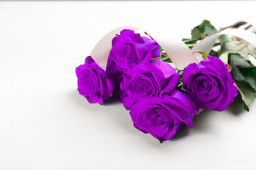 Violet roses on white wooden table, space for text. Funeral attributes
