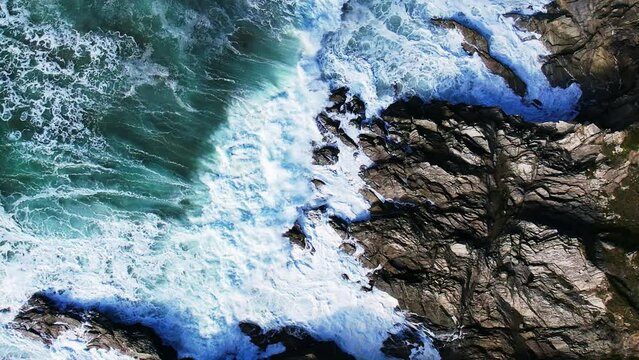 Atlantic Waves in Slow Motion Crashing Over Cornish Rocks with White Water Splashing. Top down View with Slow Rotating Shot.