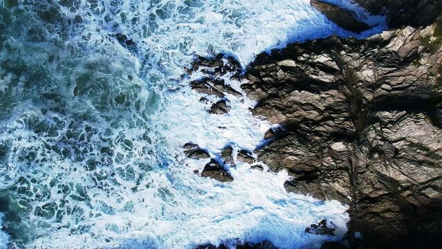 White Ocean Waves in Slow Motion Over Cornish Rocks in Cornwall, UK. Top Down View with Slow Spinning Movement.