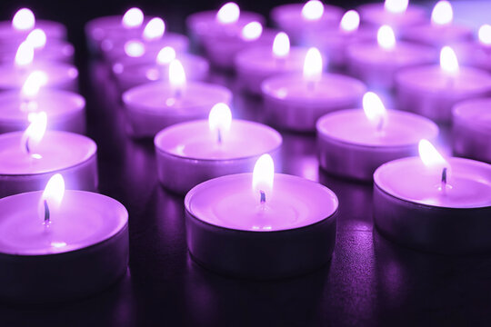 Beautiful burning violet candles on black background, closeup. Funeral attributes