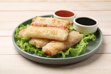 Delicious fried spring rolls and sauces on light wooden table