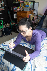 Mujer joven latina con lentes acostada en su cama estudiando en la tableta