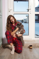 A pregnant woman in the living room with cup of tea sits on the threshold of a glass door and plays...
