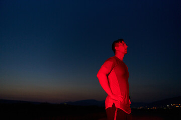 Athlete Strikes a Pose Under Red Nighttime Glow After Intense Daylong Marathon.