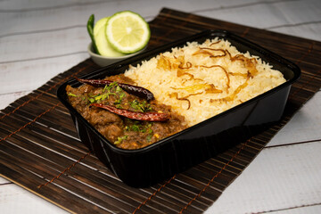 Achari beef pulao biryani rice with cucumber and lemon slice served in dish isolated on wooden table side view of bangladeshi and indian spicy food