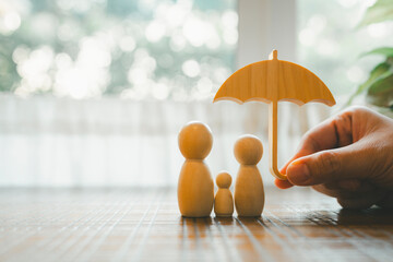 Parent and child model holding an umbrella on a wooden table, concept of health insurance, life and savings insurance