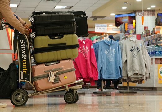 Miami, Florida, U.S.A - February 24, 2024 - The stack of luggage on the trolley in front of the souvenir shop at the airport