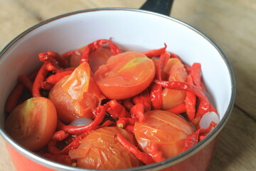 Chili, tomatoes and onions stewed in a red pot on the table