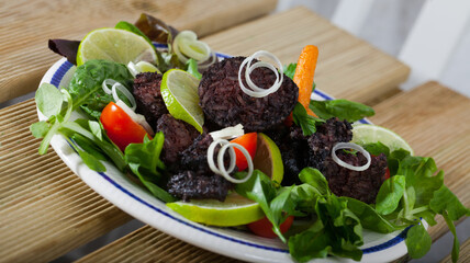 Appetizing black pudding with rice served with vegetables and greens on plate
