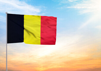 3D illustration of a Belgium flag extended on a flagpole and in the background a beautiful sky with a sunset