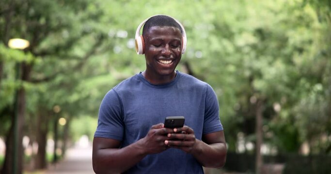 Phone, fitness and happy black man in a park walking with headphones, music or chat in nature. Smartphone, search and male runner in a forest with app for workout tracking, progress or exercise goal