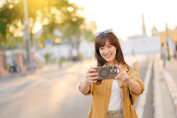 Traveler asian woman in her 30s using smartphone to take a photo while traveling urban street in Bangkok, Thailand