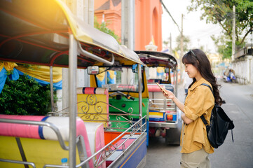 Young Asian woman backpack traveler standing a side of Tuk Tuk taxi on summer vacations at Bangkok,...