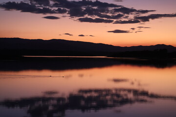 Colourful sunset over a flat lake with mountains in the background and clouds reflecting in water while birds swim