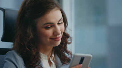 Fototapeta premium Smiling woman receiving message on modern smartphone sitting workplace close up.
