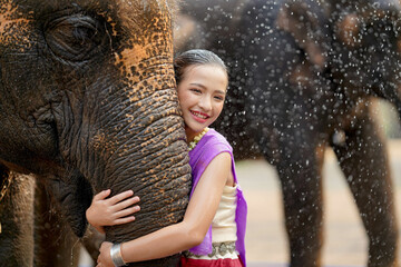 Beautiful rural Thai girl wear Thai northern traditional dress hug trunk of Asian elephant with...