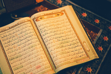 Obraz premium The Quran is opened for reading and placed on a prayer mat and has the golden glow of fire. Selective focus.