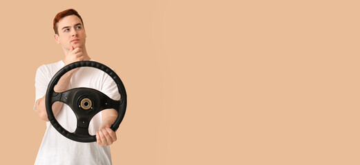 Thoughtful young man with steering wheel on beige background