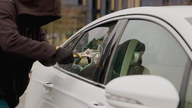 A white car in the parking lot with the window broken by a thief using a key as he reaches through the hole in the broken window to retrieve a woman's aba bag, daring act of theft