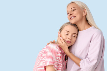 Happy young beautiful woman with her mother hugging on blue background