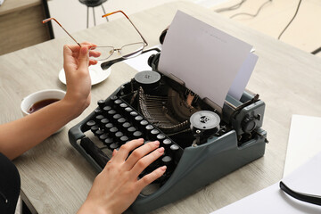 Woman typing on vintage typewriter at beige wooden table
