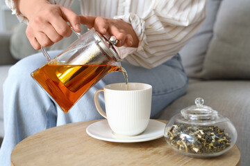 Young woman pouring hot tea into cup at home, closeup