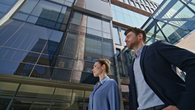 Two corporate workers standing urban street looking at distance bottom view.