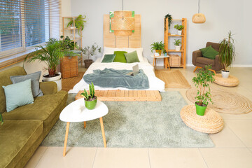 Interior of bedroom with green plants, shelf units and laptop on bed