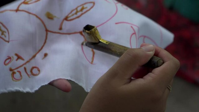 4k footage of participants learning to make traditional batik using hot wax in a pan and canting drawn on a piece of white cloth. The process of beginners learning to paint traditional Javanese batik