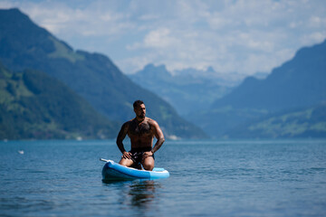 Man on paddle board in Alps lake mountains. Leisure activities with paddle on Lake in Switzerland. Man paddle surfing board on Geneva Lake. Muscular sexy strong Hispanic man paddle board surfers.