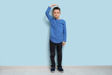 Cute little boy measuring height near blue wall