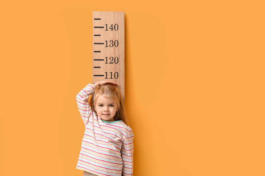 Cute little girl measuring height on yellow background