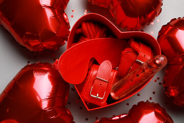 Gift box with different sex toys and heart shaped air balloons on grey background. Valentine's Day...