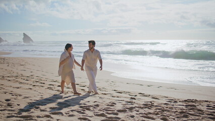 Joyful spouses enjoy seashore stroll having fun expecting baby. Couple walking