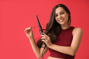 Obraz premium Beautiful young woman with curling iron on red background