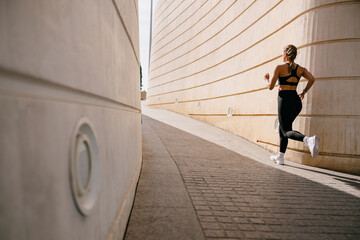Back view of woman in sportswear is running on modern buildings background. Active lifestyle concept