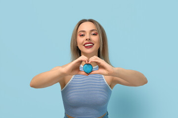 Beautiful young woman with blue sweet macaroon heart shaped gesture on color background