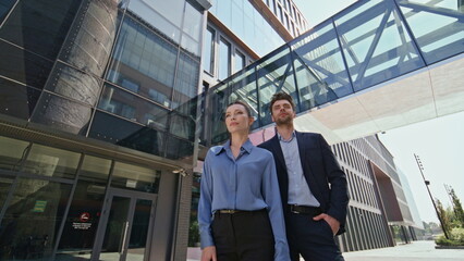 Portrait couple office employees outside contemporary office building zoom in. 